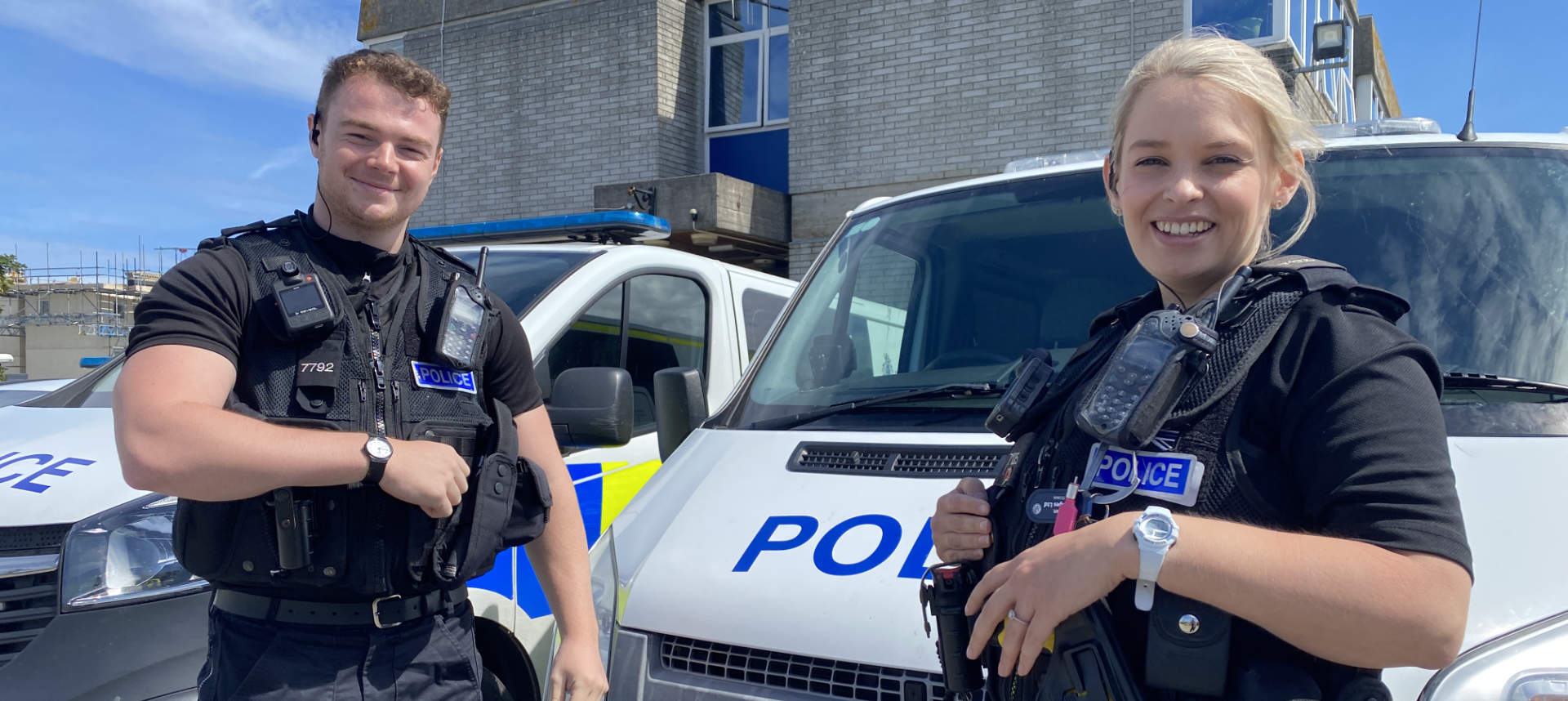 Male and Female officer in uniform smiling in front of Police vehicles. 