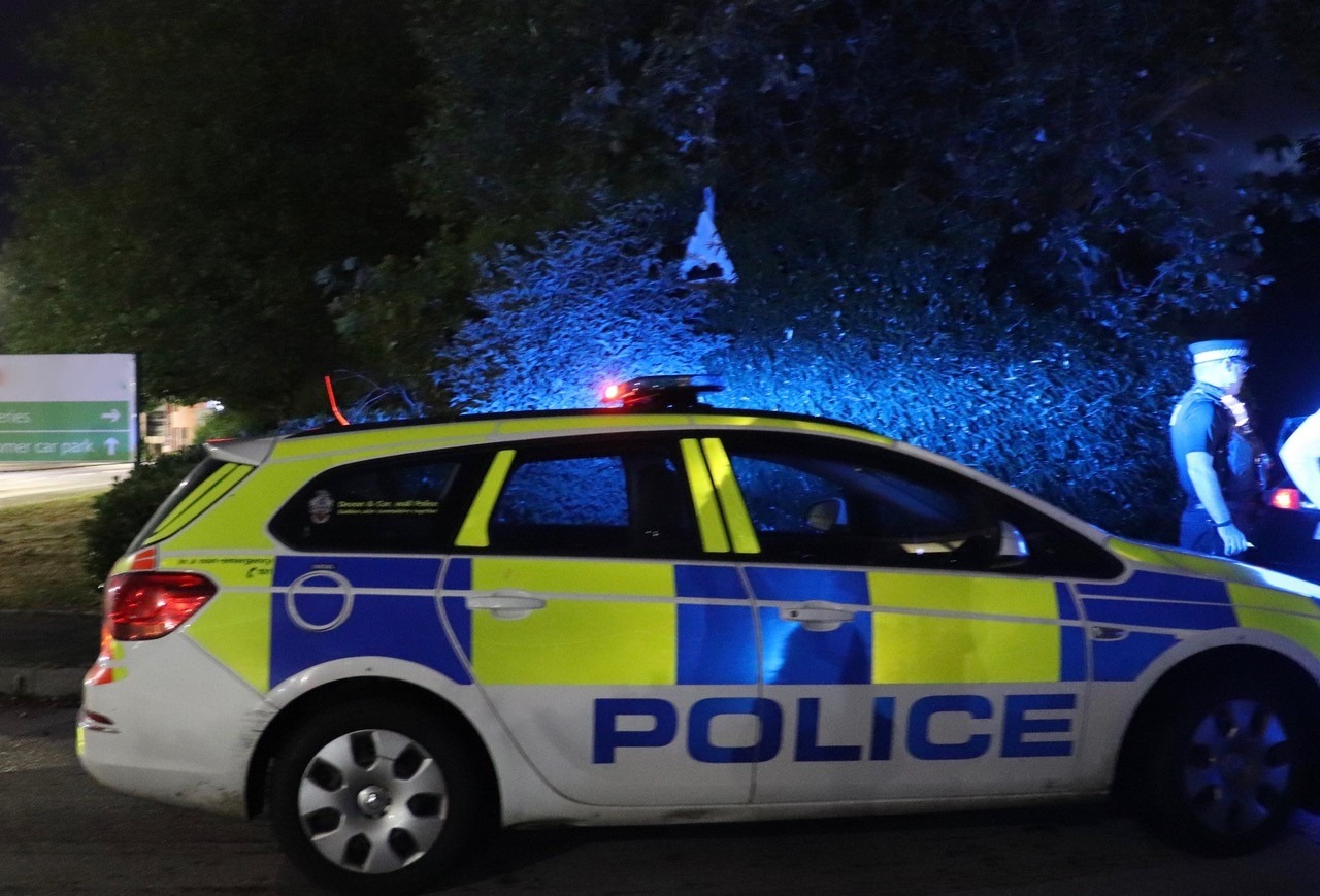 An officer on his radio standing next to his Police car with its blue lights on at night