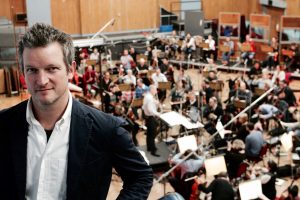 Barnaby Taylor standing with an unfocus orchestra behind