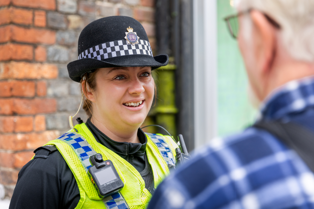 Male police officer smiling leaning on countryside fence