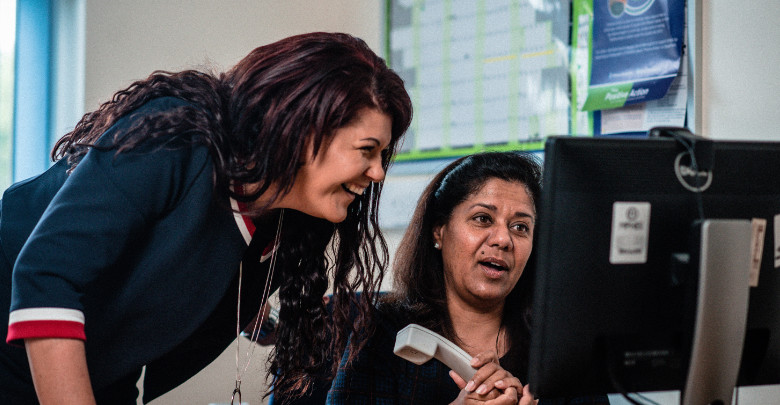 Two staff members smiling while looking at a monitor