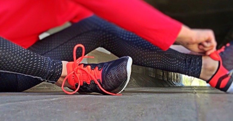 Someone in a red top sat on the floor tying up her shoe laces