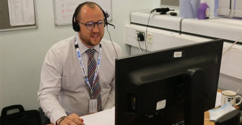 A person sat at a desk with a headset on looking at a computer screen