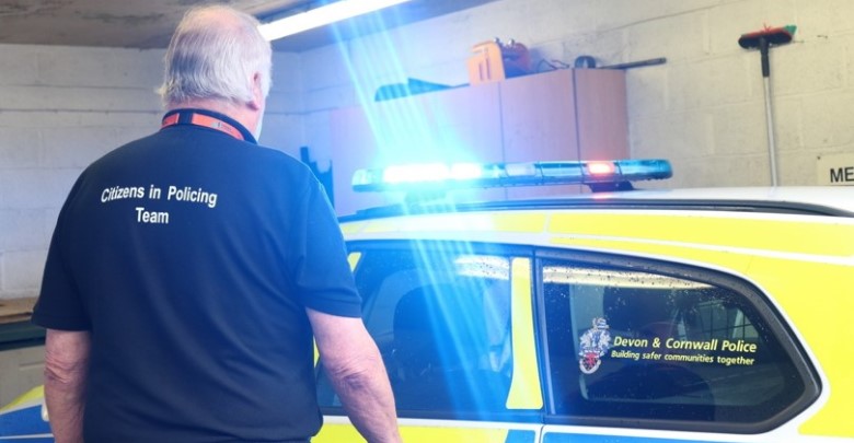 A volunteer walking towards a police car with its lights on in the workshop