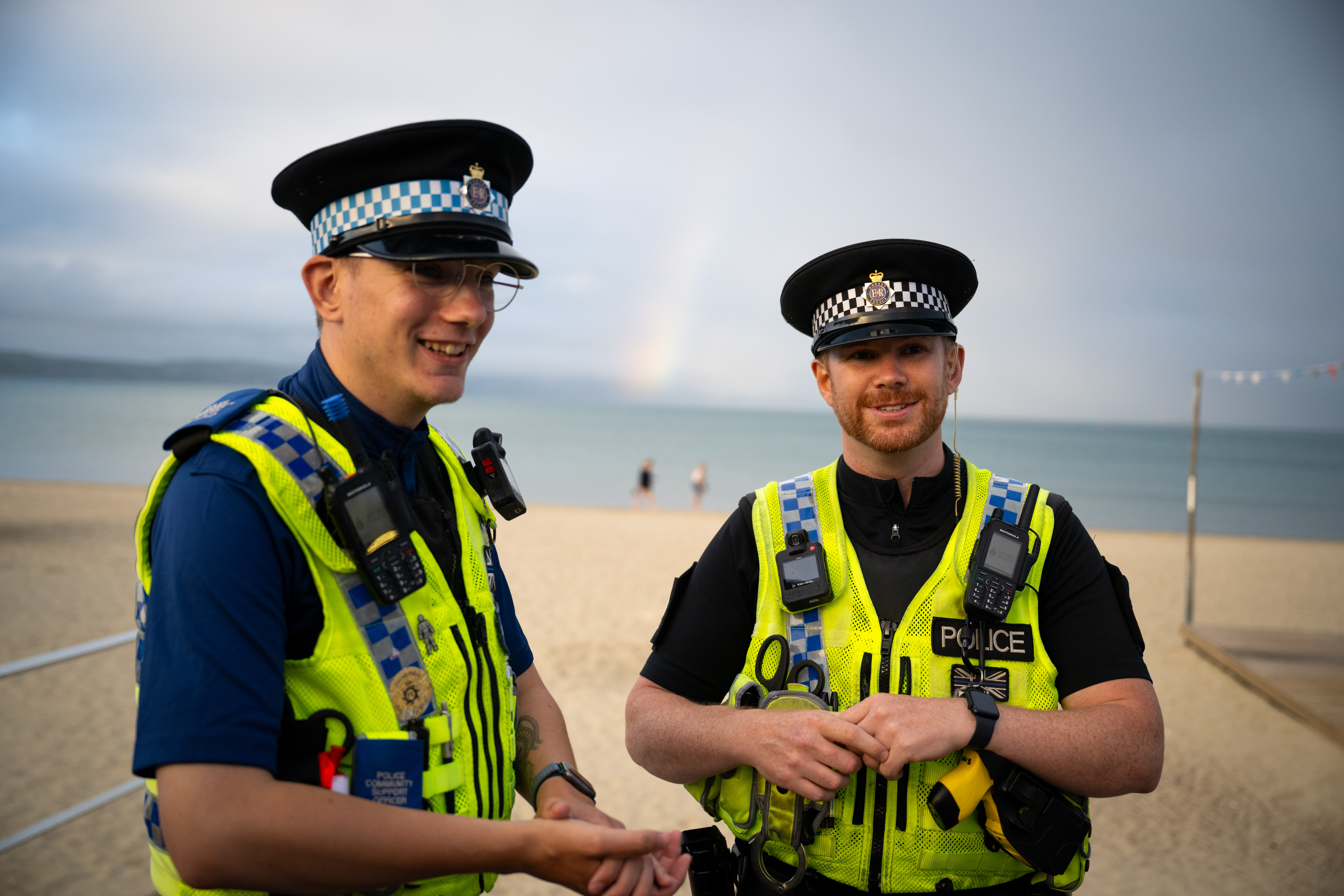 A male PCSO and male police officer smiling standing on the beach