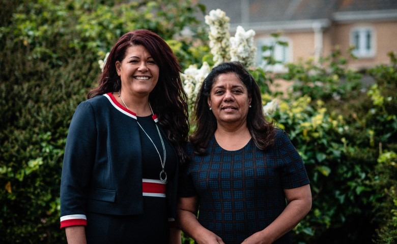 Two female staff members stood infront of hedge